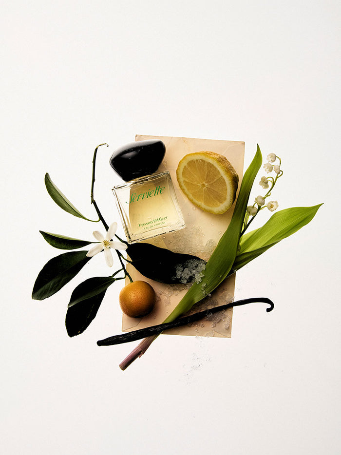 Perfume bottle with bergamot, vanilla bean, and flowers on a white background