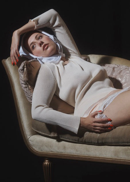 Woman lying in repose on settee with hand over brow wearing a cream jumper.