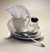 Serviette bottle leaning on charger plate with jug and spoon.